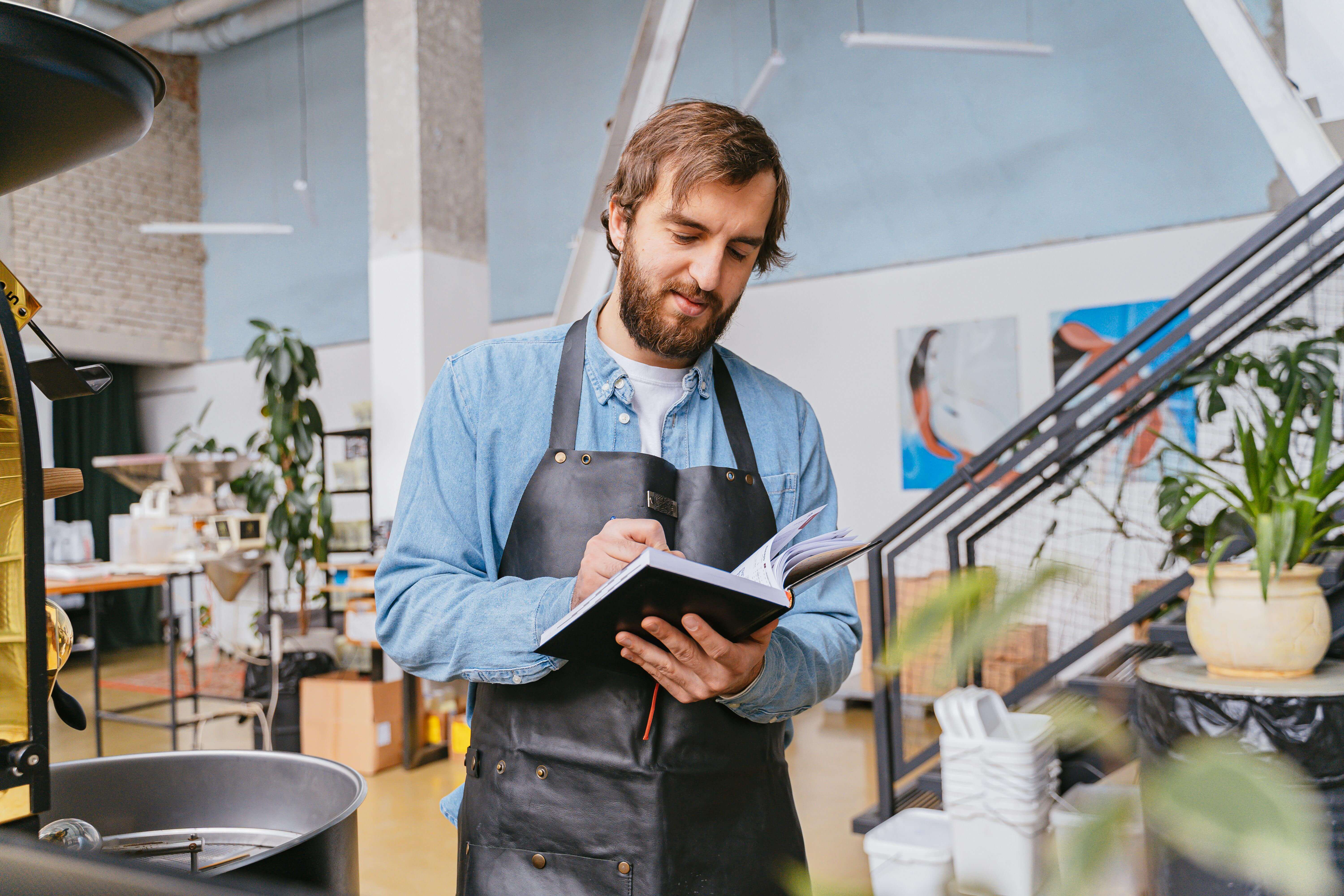 Man wearing black apron writing on a notebook.