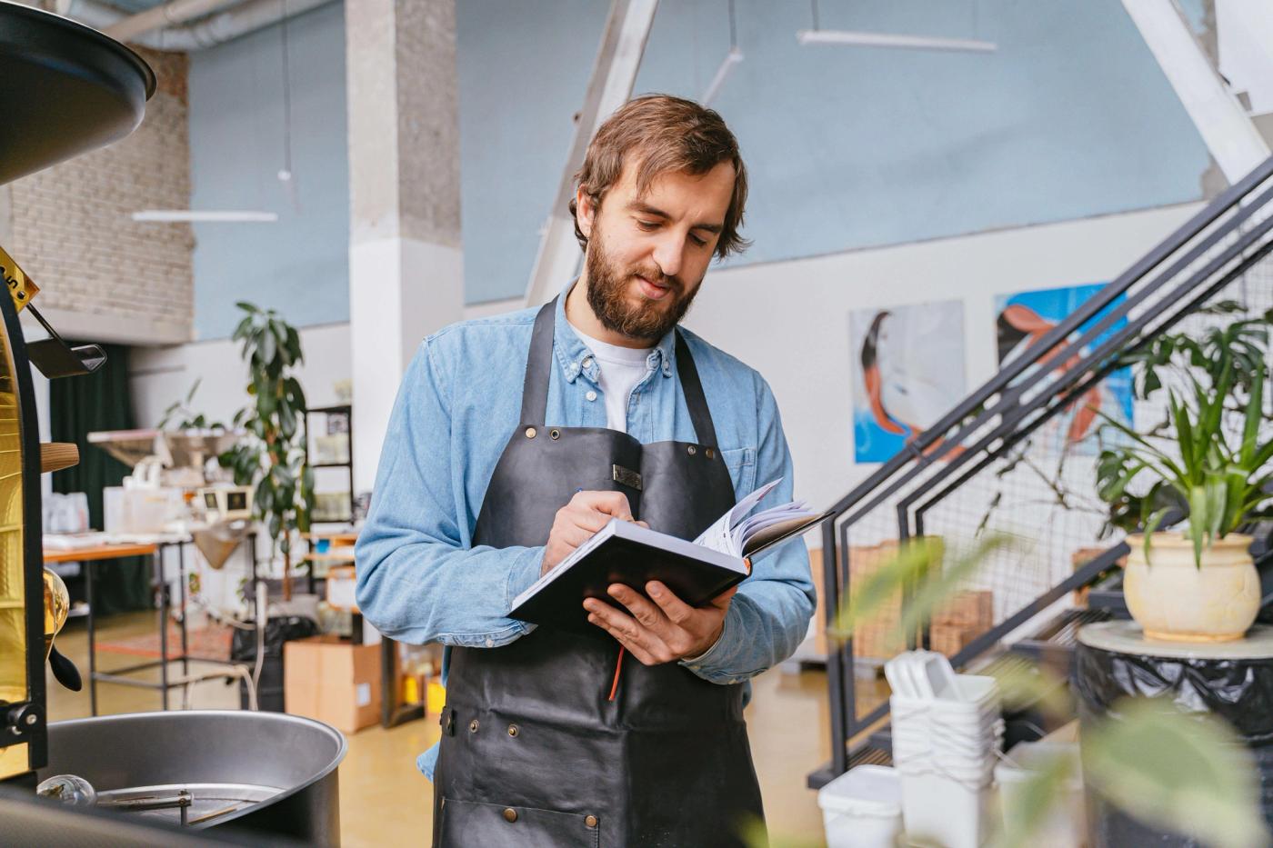 Man wearing black apron writing on a notebook.