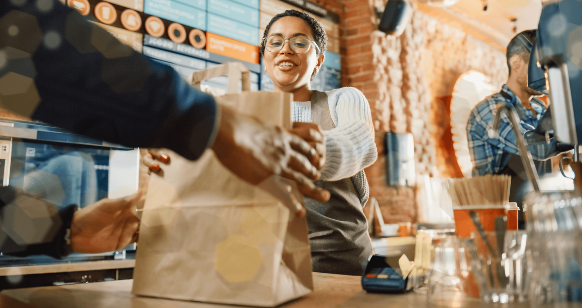 Restaurant staff handing a takeout order to a customer.
