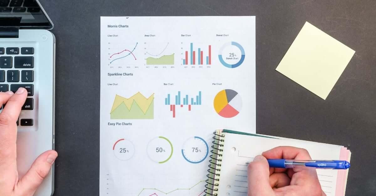 A laptop, chart, notebook, and pen laid out on a table.