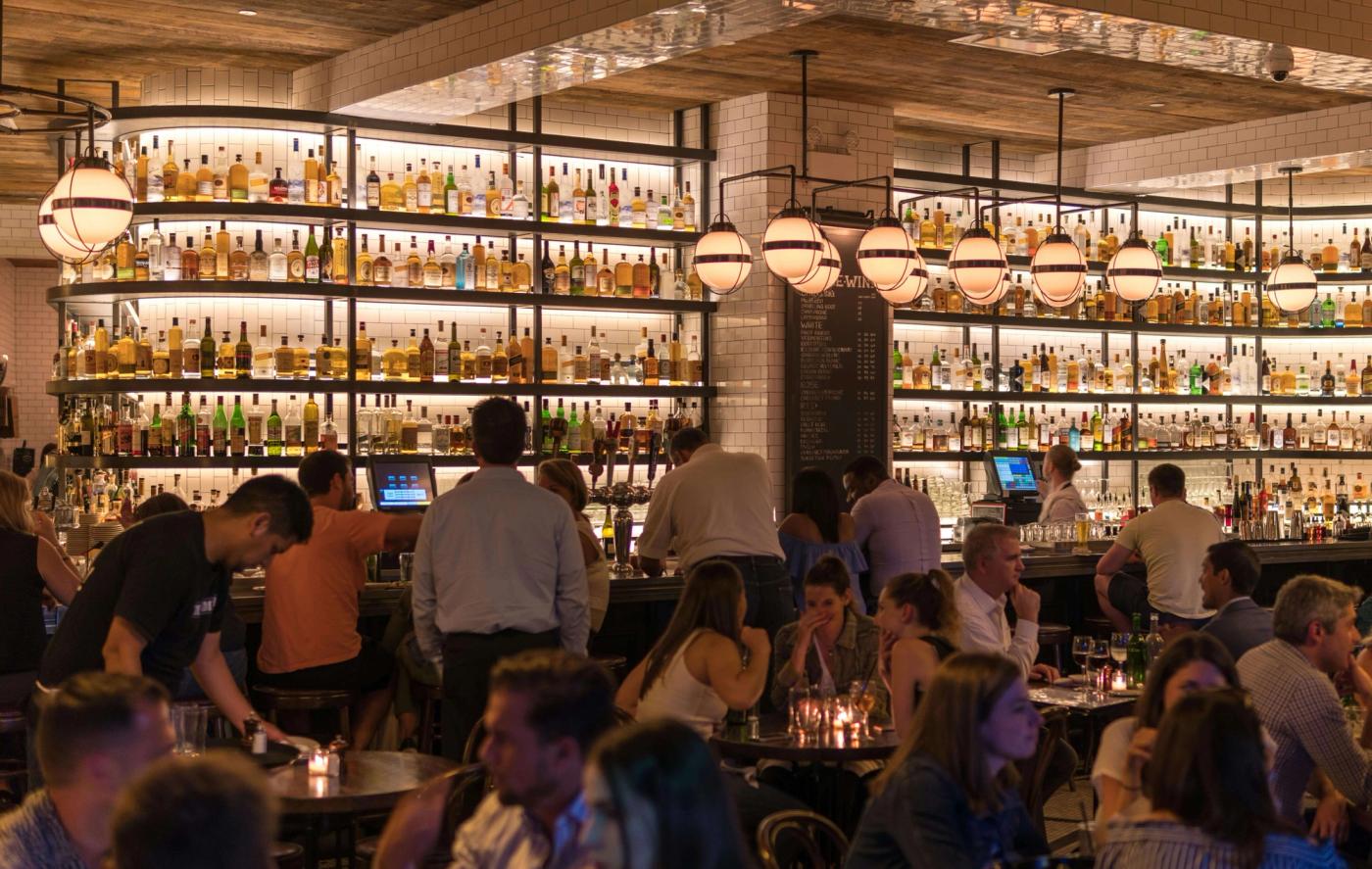 A crowded bar scene filled with numerous people seated at tables, enjoying drinks and conversation.