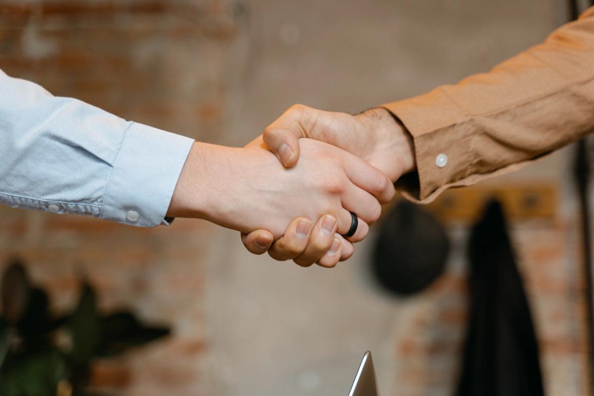 Two individuals sealing a deal with a handshake over a laptop.