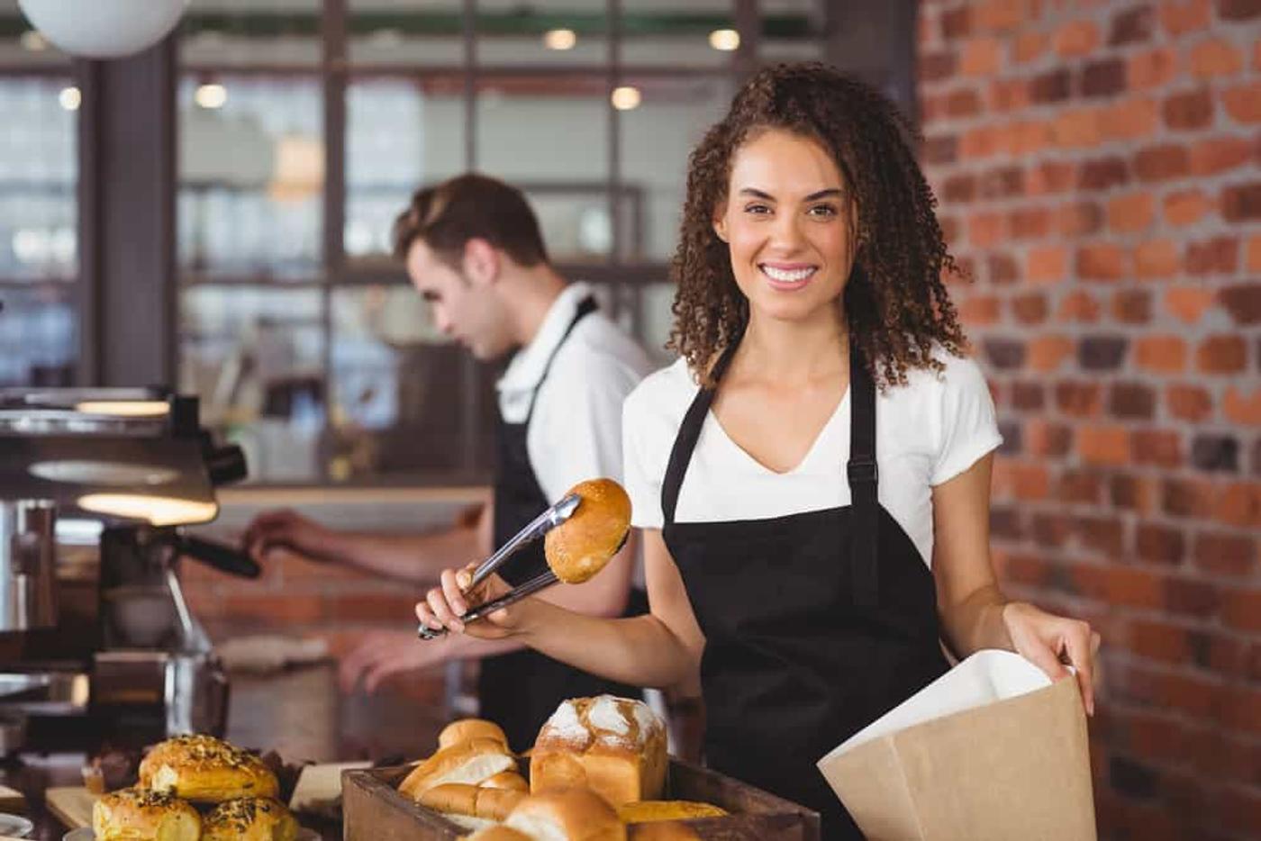 A woman in a black apron holding a bread using a thong.
