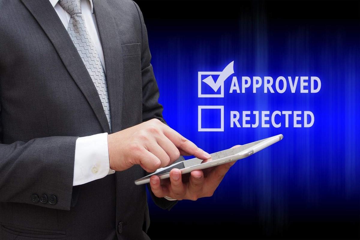 A man holding a tablet with an ''approved" and "rejected" in the background.