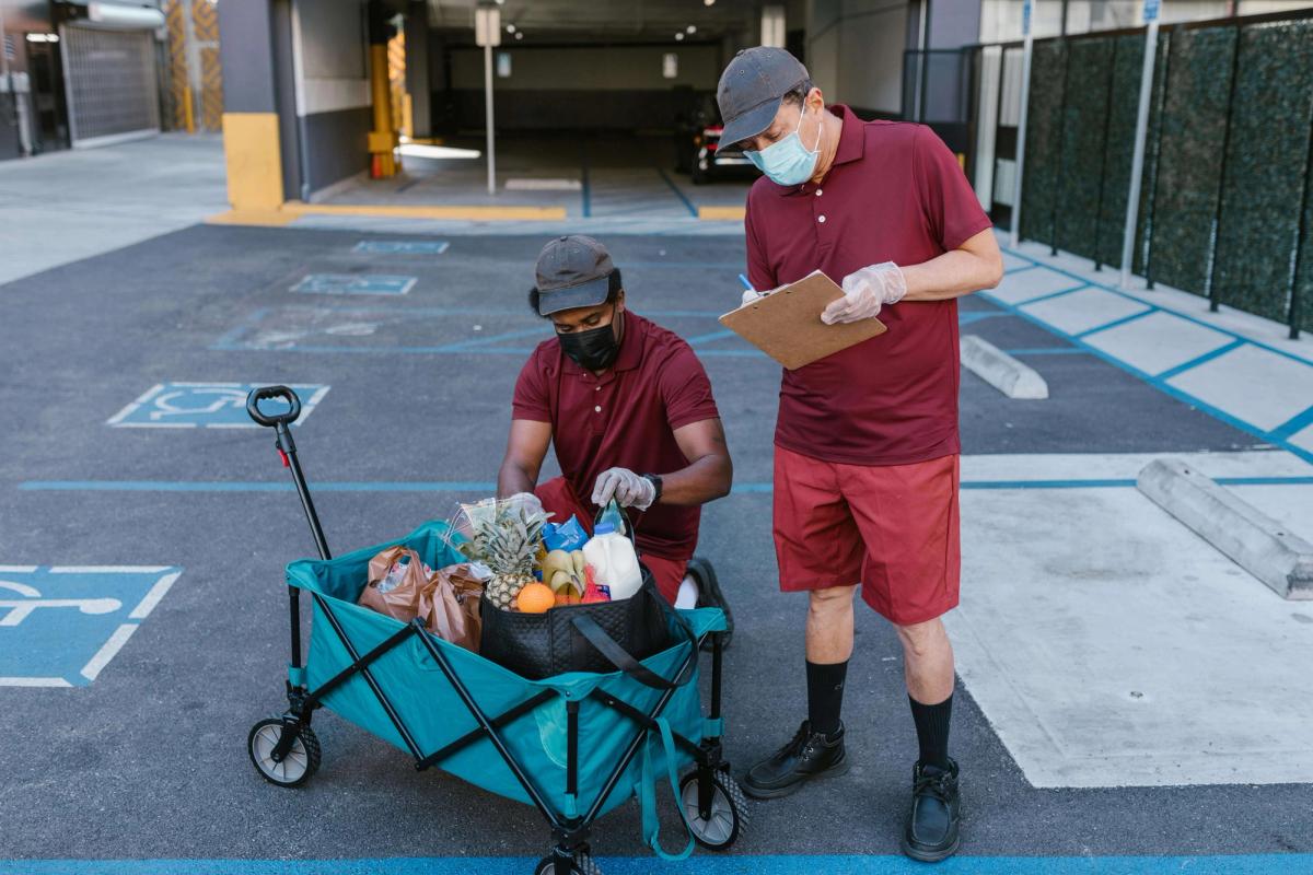 Man in red crew neck t-shirt and black pants holding black and gray stroller.