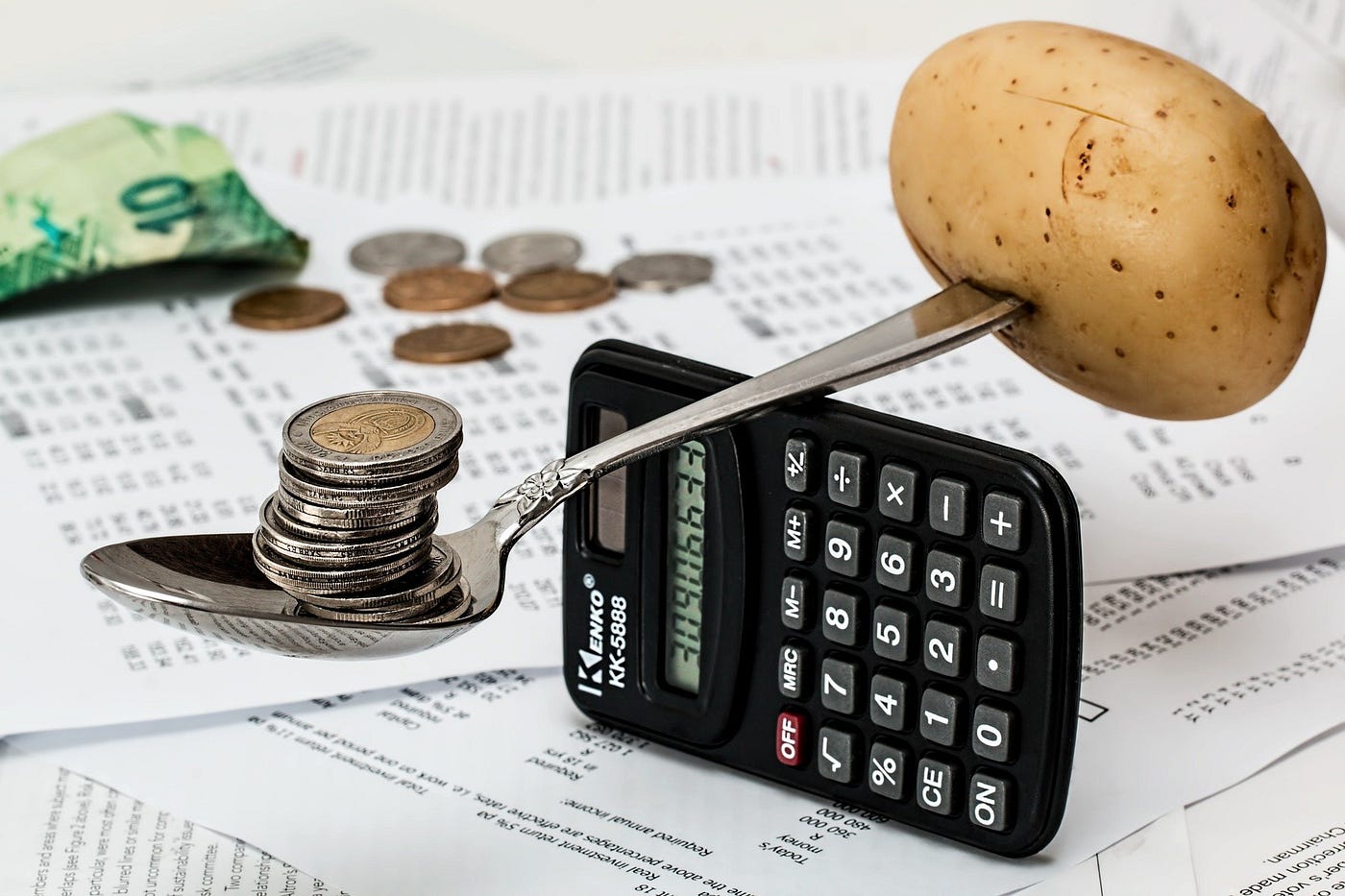 A potato and coins are placed on a calculator, representing a quirky blend of budgeting and food resources.