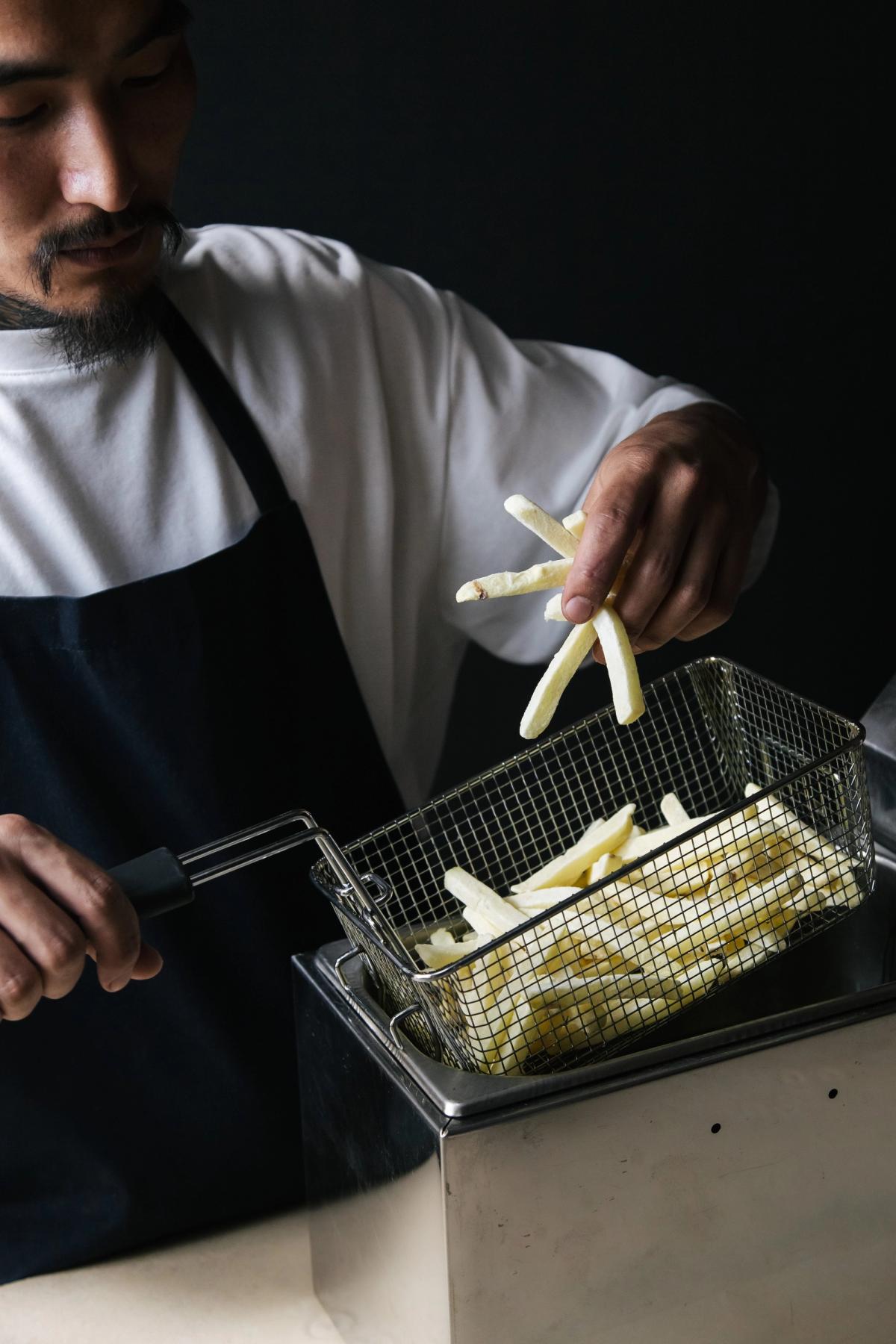 A man in an apron frying french fries.