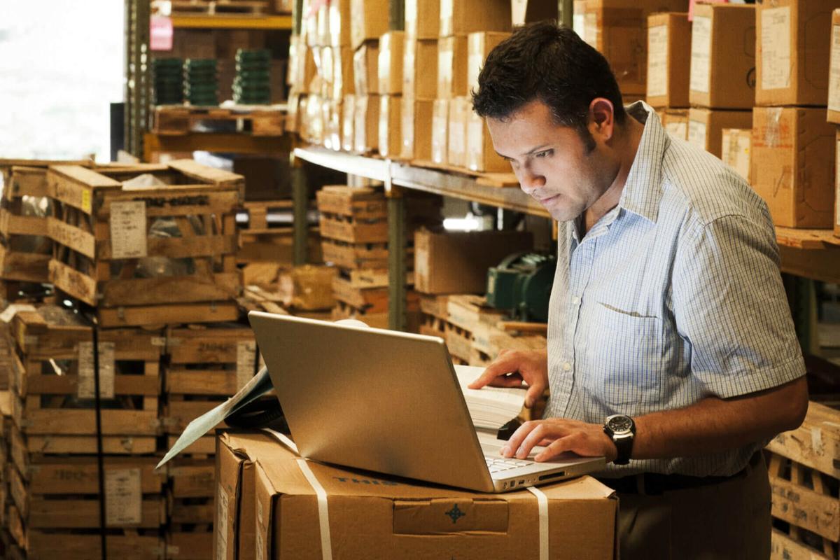 A man checking inventory using his laptop in a warehouse.