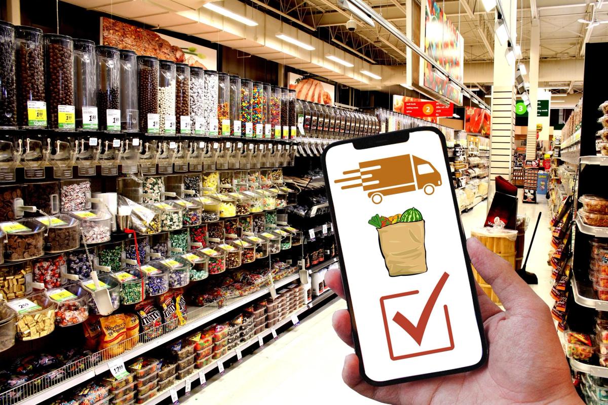 A person holding a cellphone in a store with an image of a delivery truck, a box of fresh produce, and a check mark.