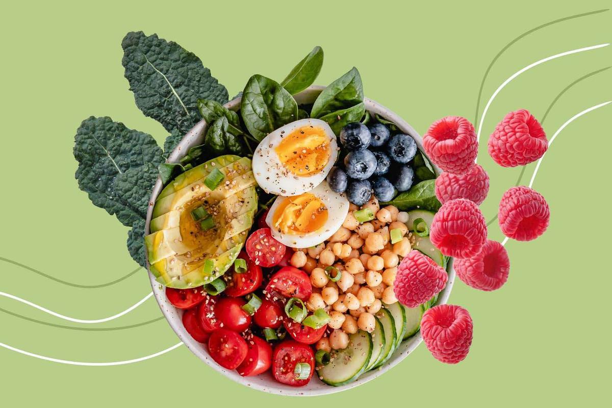 A bowl filled with fresh raspberries, eggs, and assorted vegetables, showcasing a vibrant and nutritious meal in a teal green background.