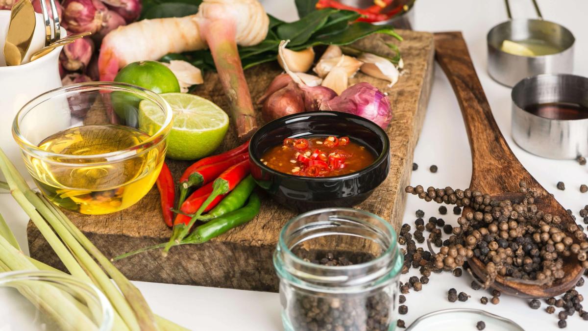 Spices for use as cooking ingredients on a wooden background with fresh vegetables.