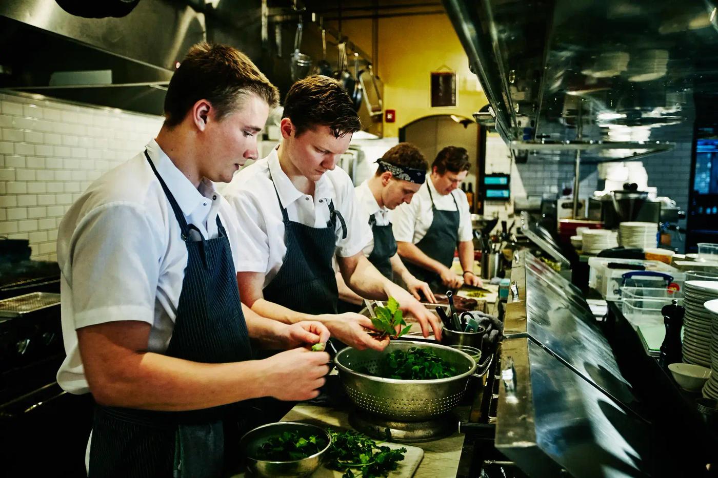 Four chefs in a kitchen preparing the dishes.