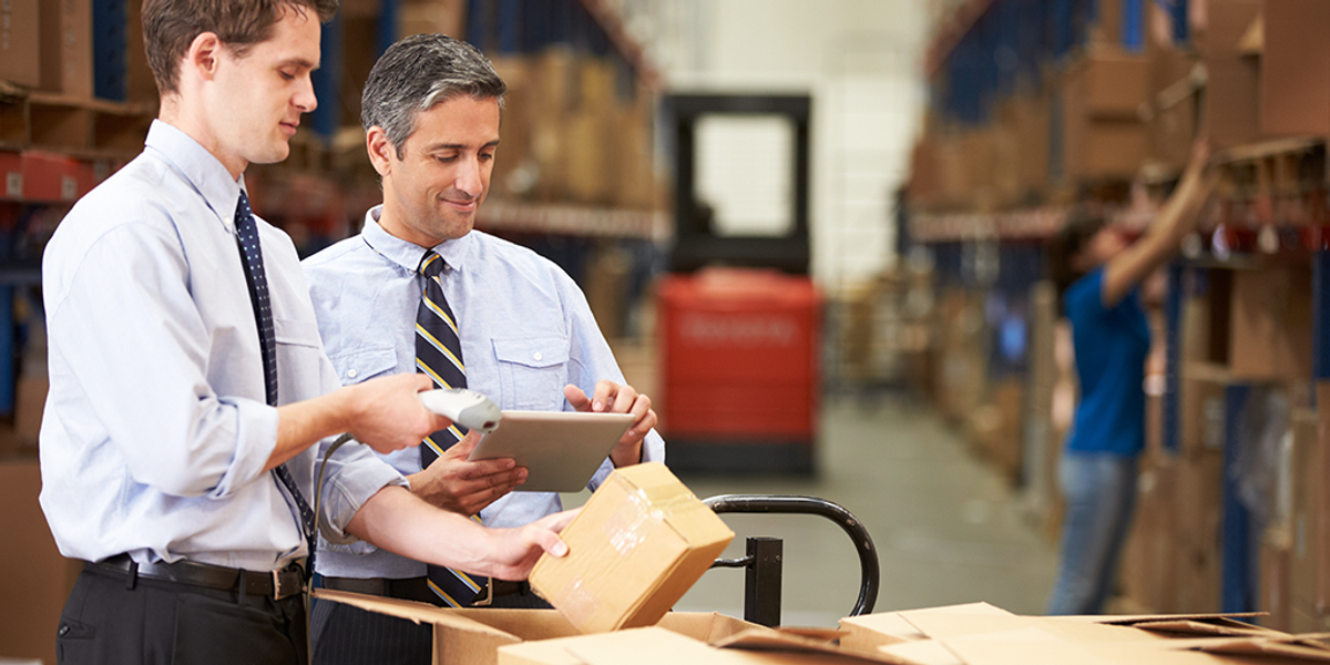 Two men wearing a necktie in a warehouse tracking the inventory using a tablet and a scanner. 
