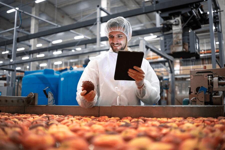 Man holding an apple and a tablet inside a factory.