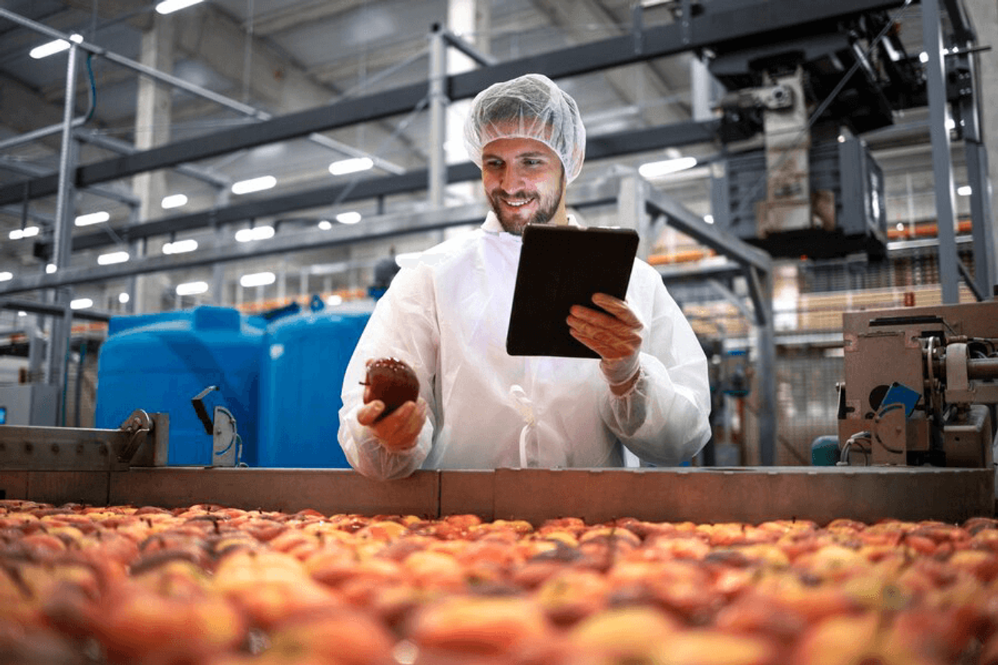 Man holding an apple and a tablet inside a factory.