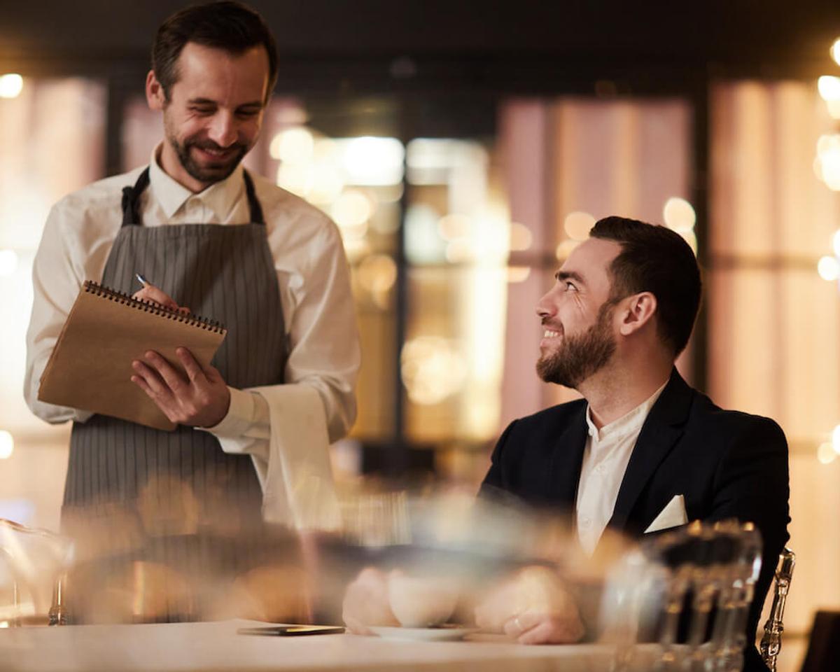 Smiling restaurant staff taking a customer’s order at the table.