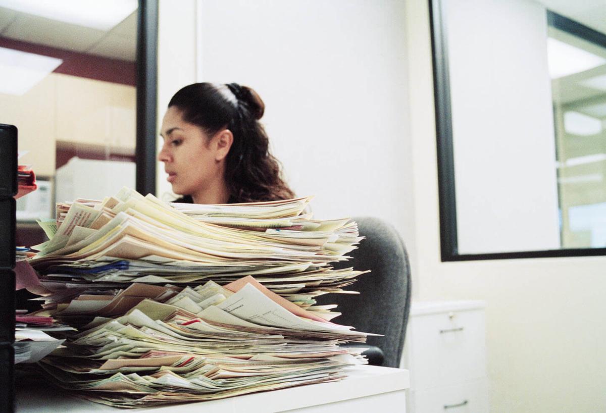 A woman sitting at a desk with stacks of papers.