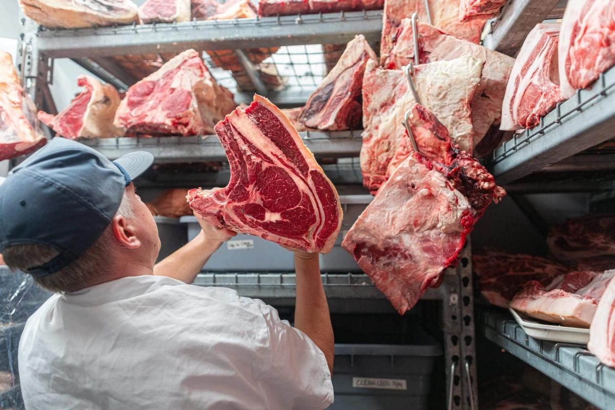 A man storing freshly cut meats into refrigerated storage.