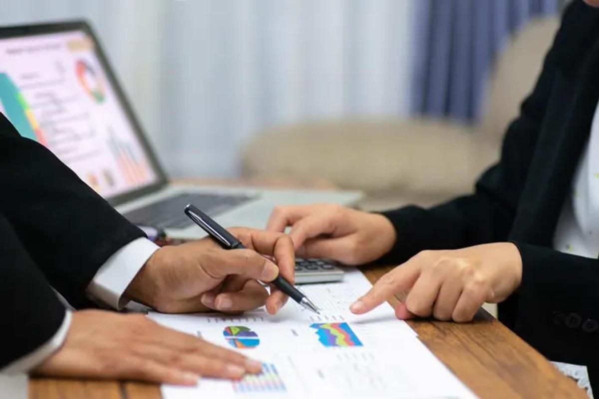 A man is holding a pen, pointing to the graph, and discussing the details with the other person at the table.
