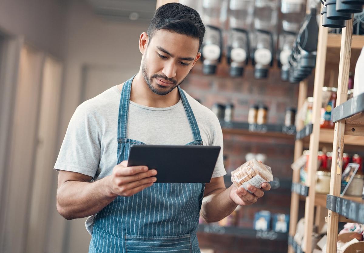 A man in a stripe blue apron using a tablet in a store to manage inventory.