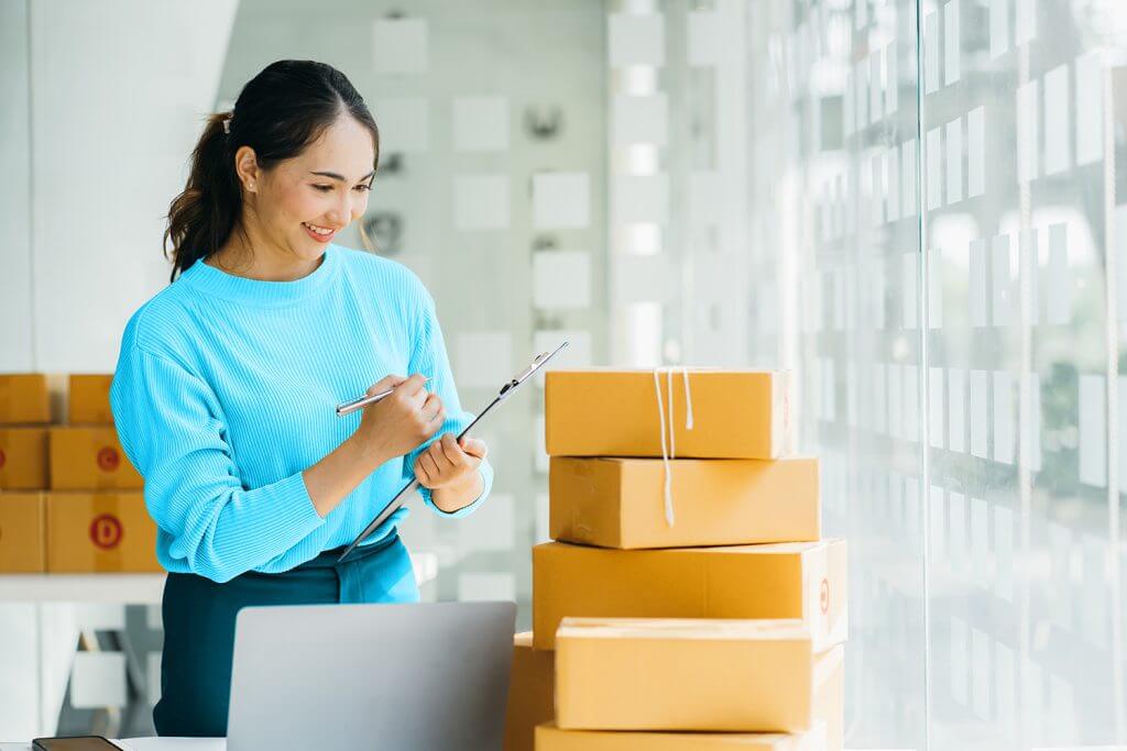 Woman checking packages beside a laptop in a bright office.