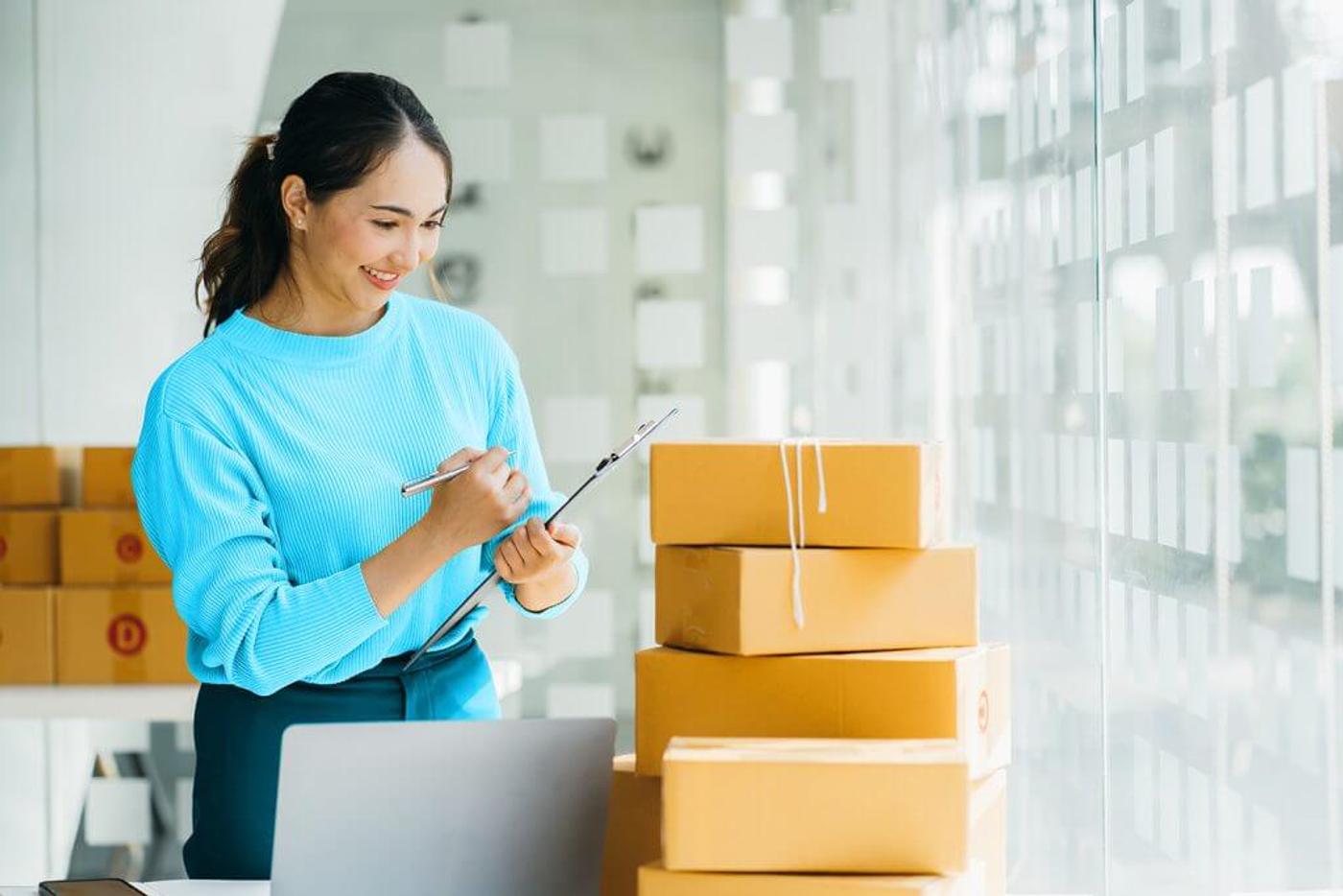 Woman checking packages beside a laptop in a bright office.