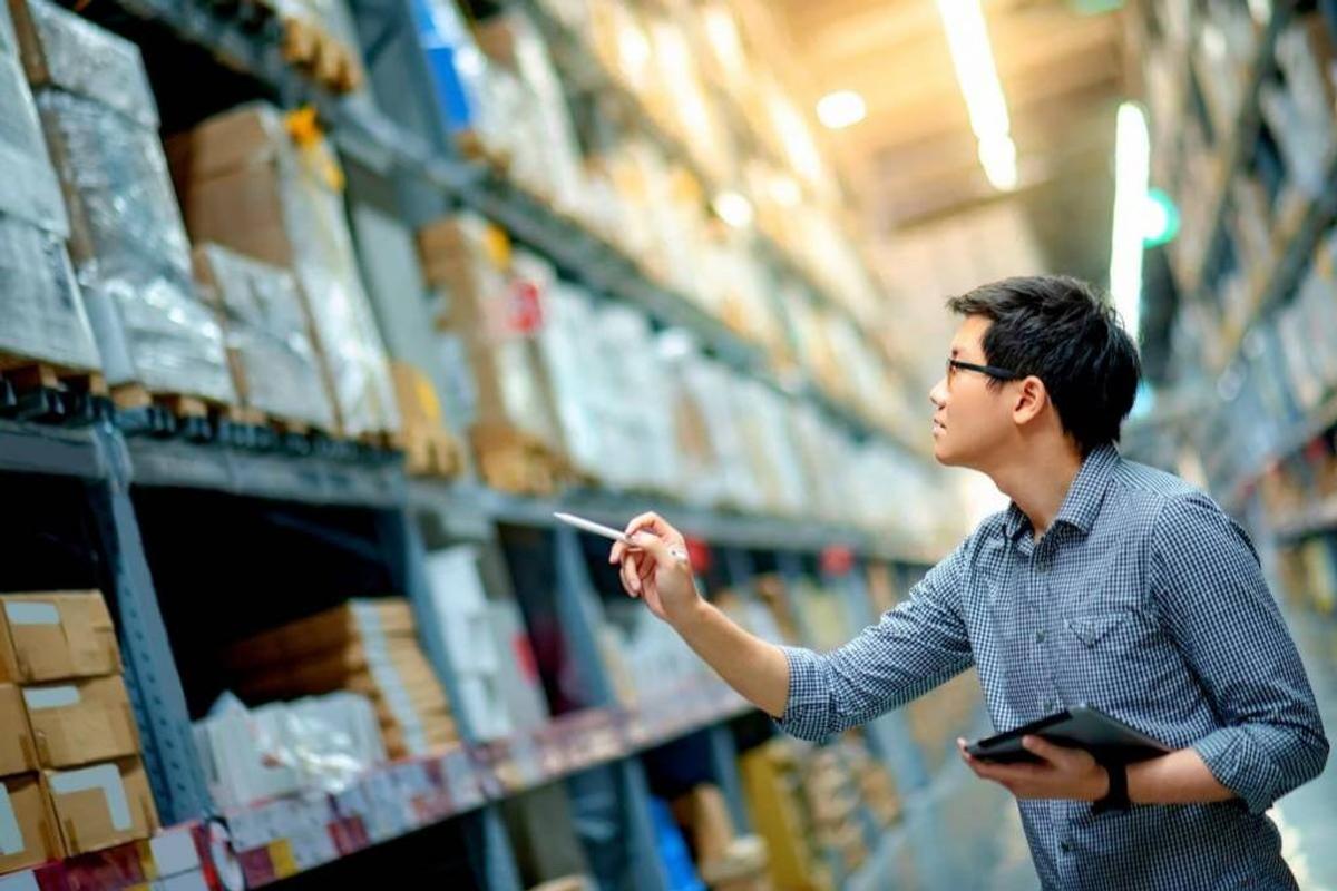 A man holding a tablet and a pen, checking the stocks in a warehouse. 