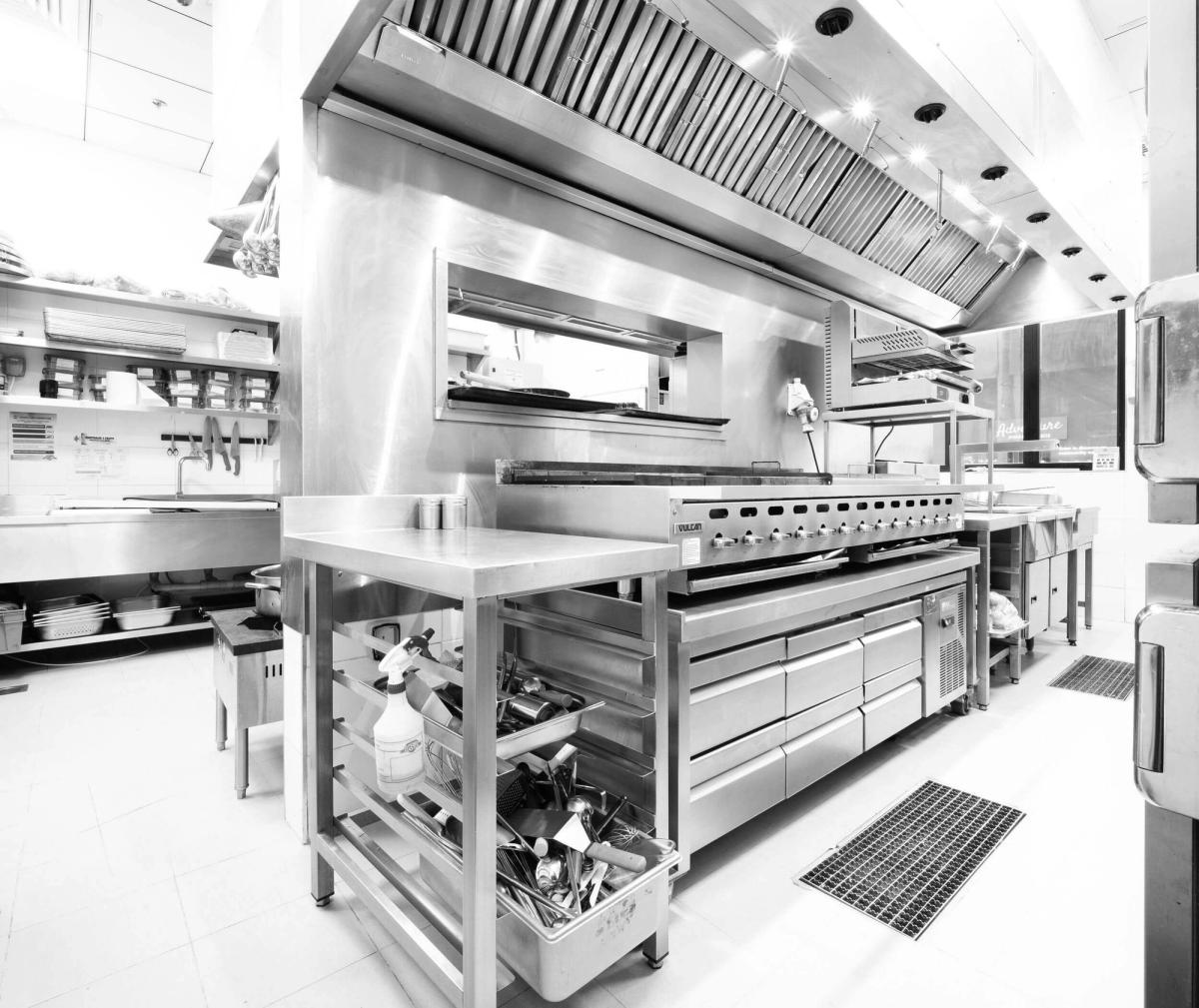 A black and white image showcasing a commercial kitchen filled with various cooking equipment and utensils.