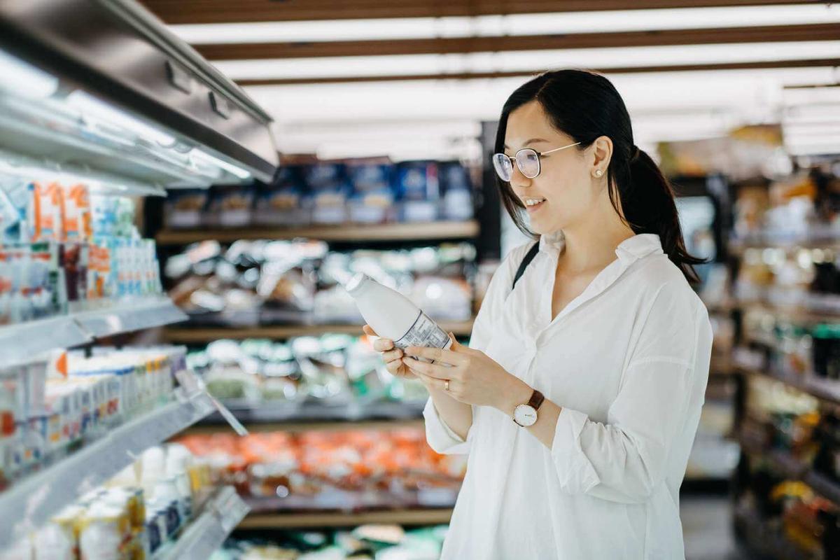 A girl holding a bottle of milk in the chilled section of a grocery store.