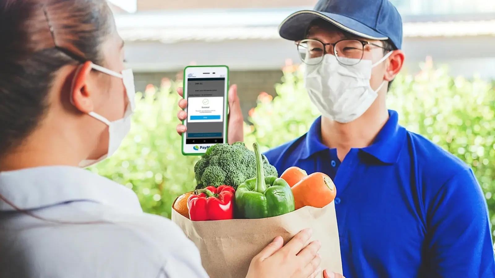 Delivery driver handing fresh groceries to a customer and showing digital payment confirmation.