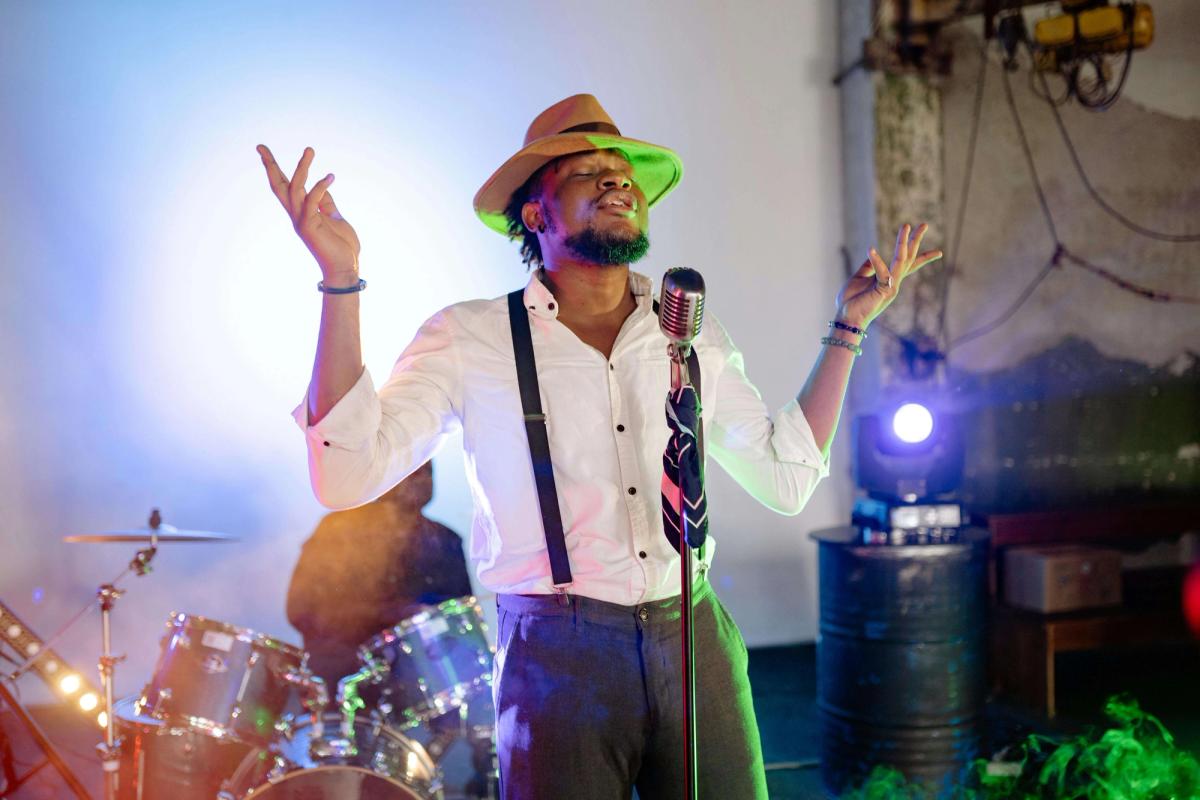A man wearing a hat, singing on stage.