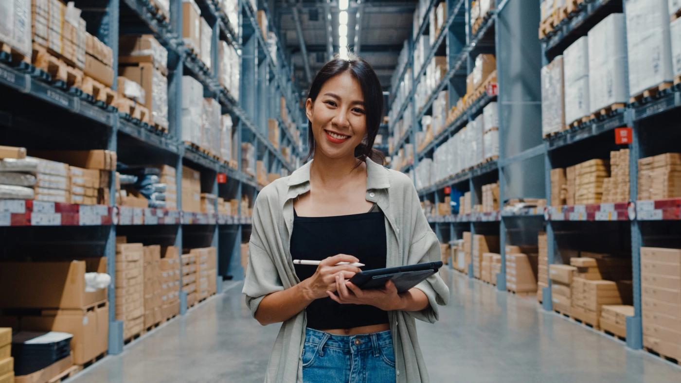 A woman in a warehouse holding a clipboard and a pen.
