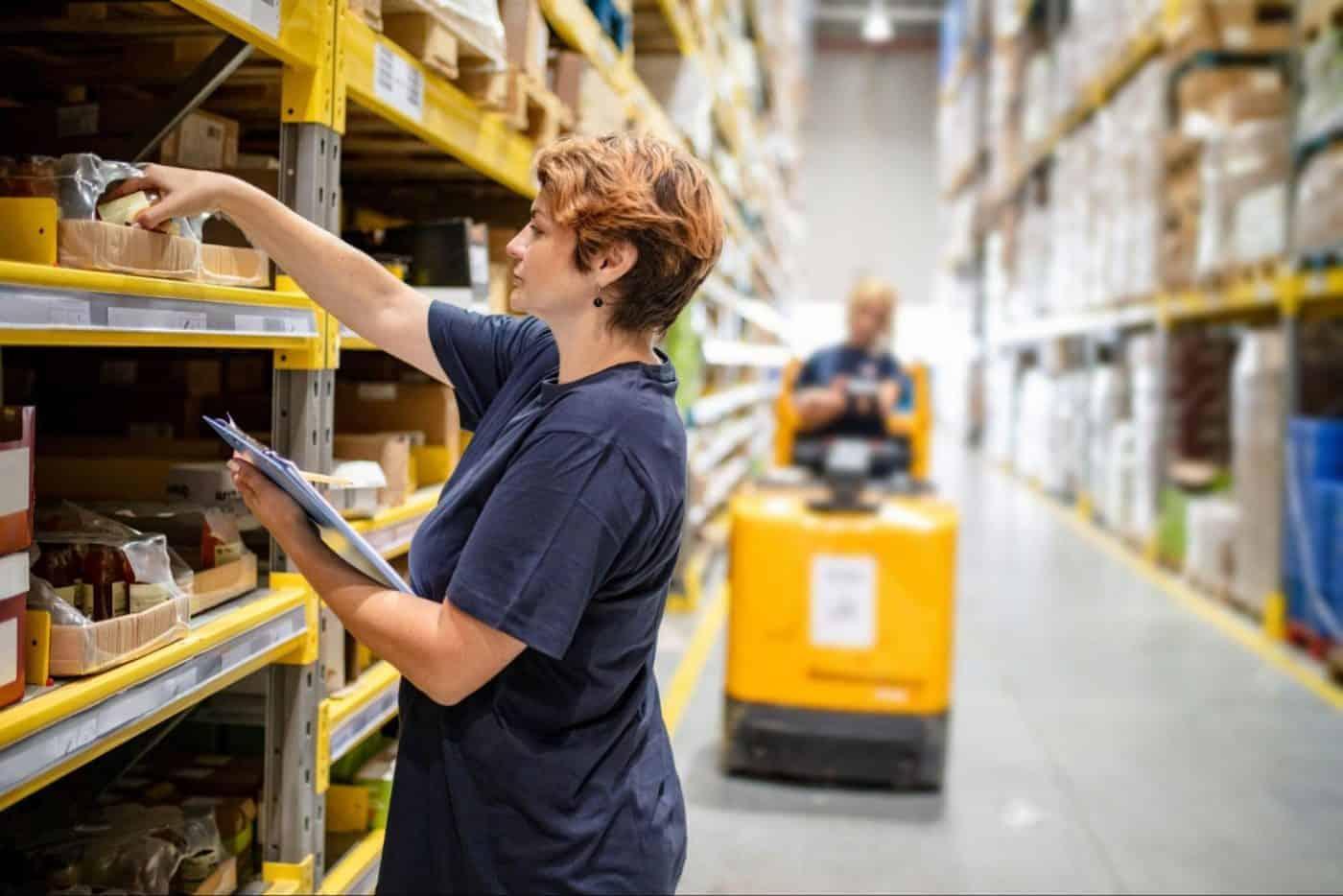 Worker picking items from warehouse shelves with a clipboard.