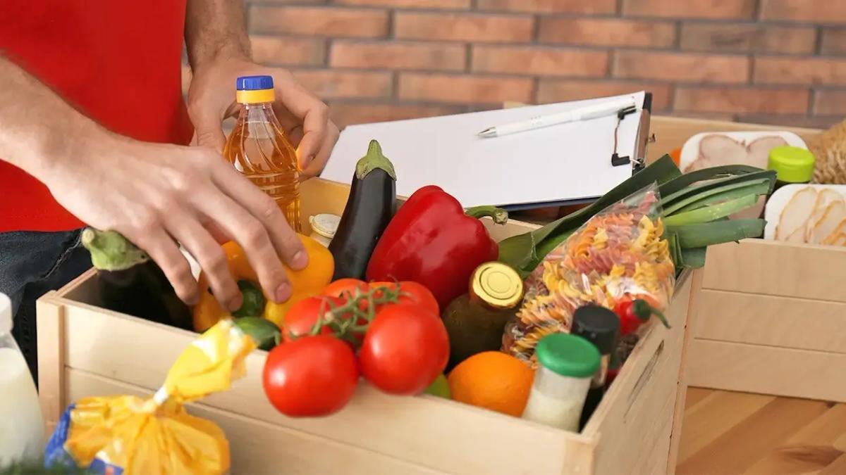 Person sorting fresh groceries in a wooden crate.