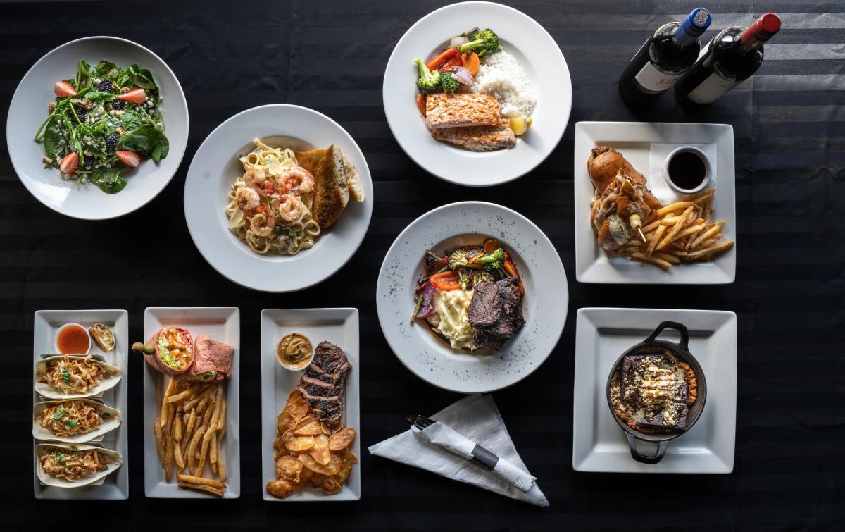 A diverse assortment of plates filled with delicious food and a bottle of wine on a table.