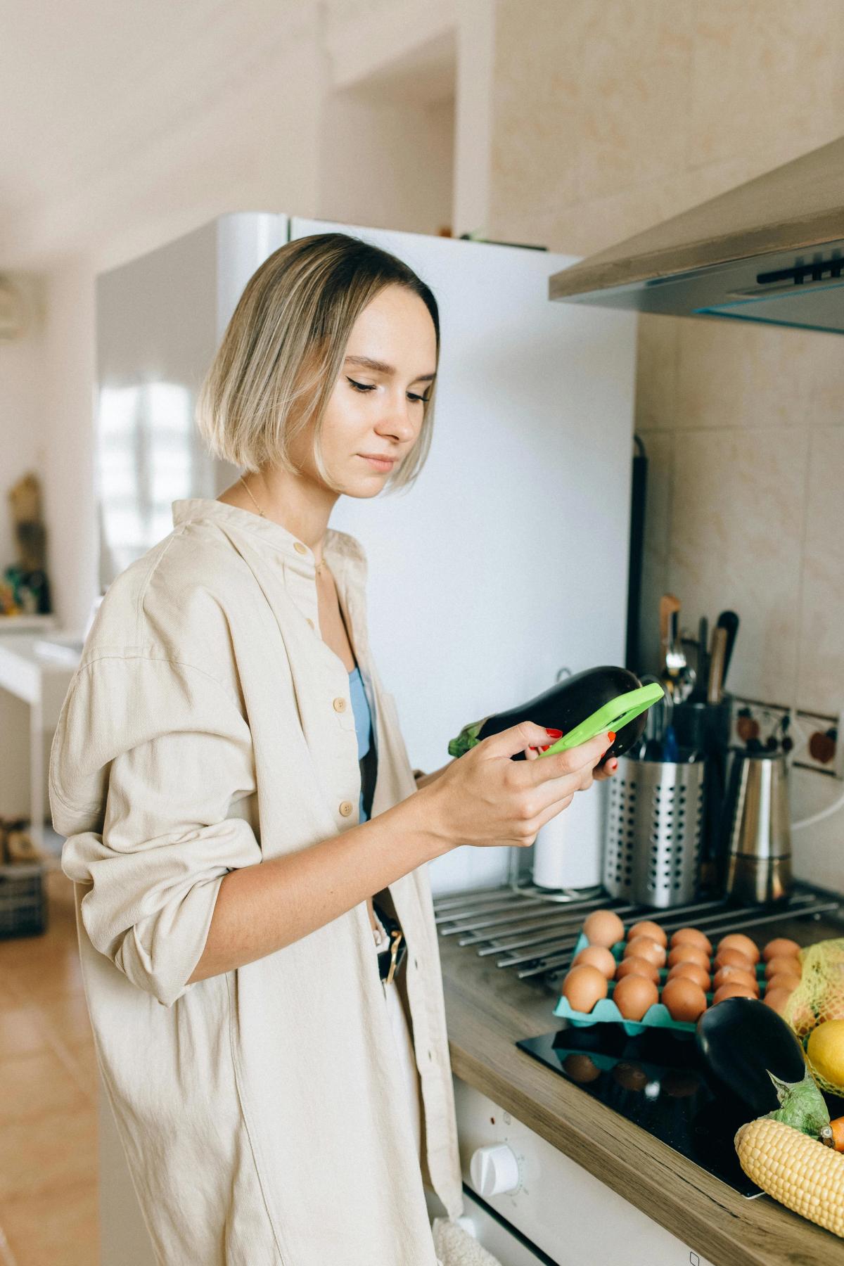 A woman standing in a kitchen looking at a cellphone.