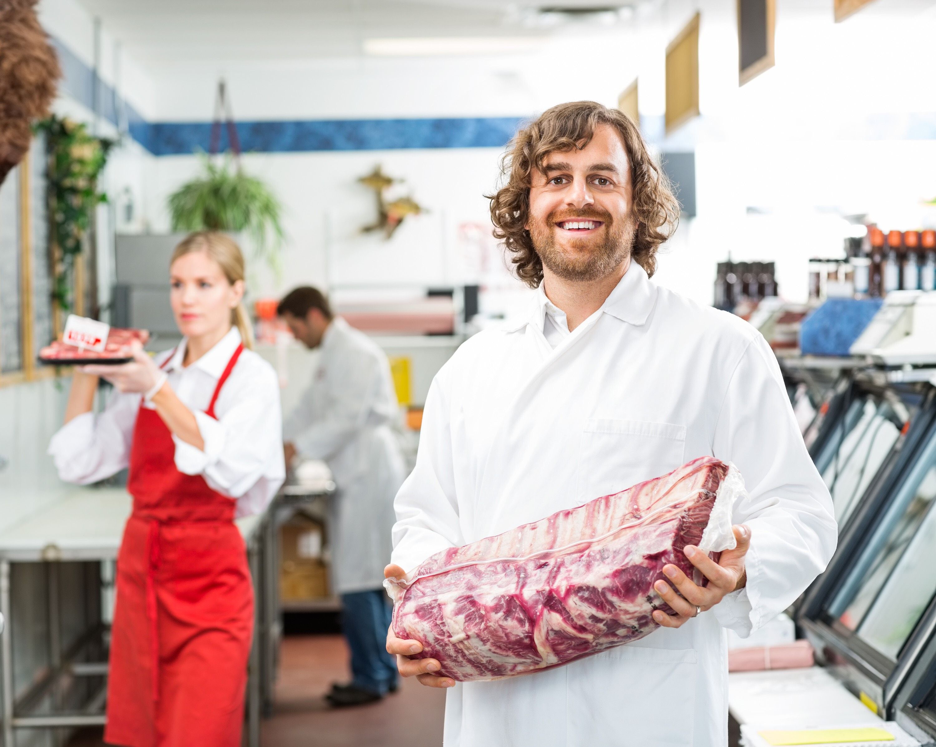 A butcher holding a cut of meat in a shop.