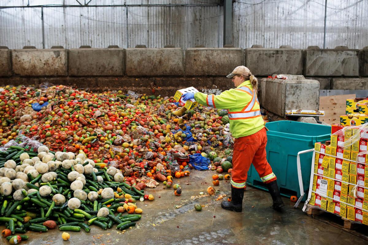 A woman disposing of food waste onto a pile of rotten vegetables.