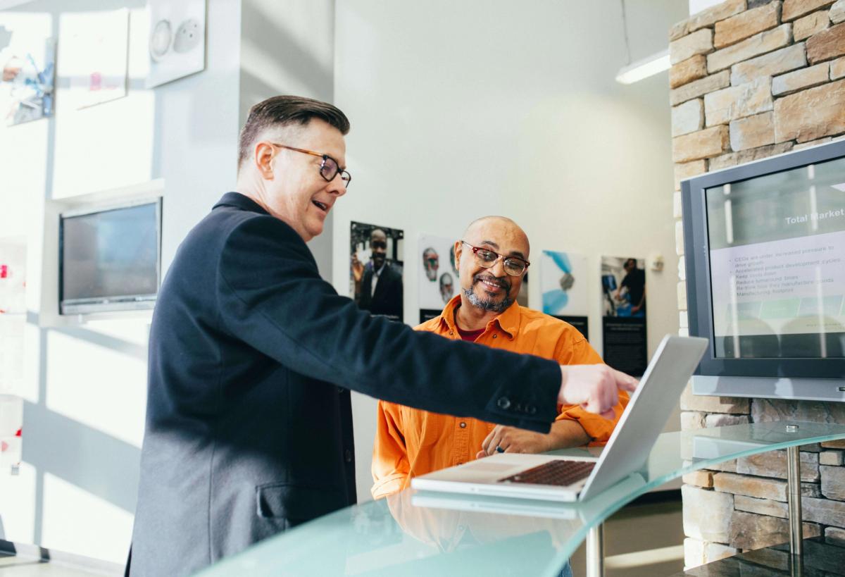 Two men discussing in front of a laptop.