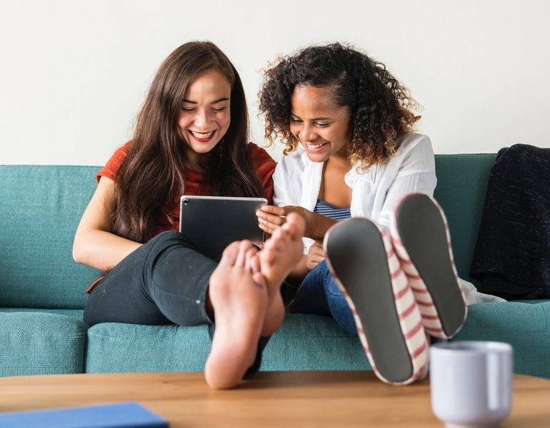 Two smiling women sit together looking at a tablet computer