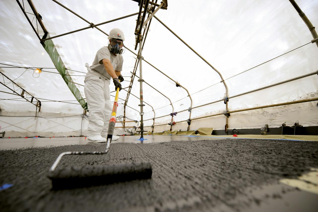 Worker rolling a surface coating onto a ship