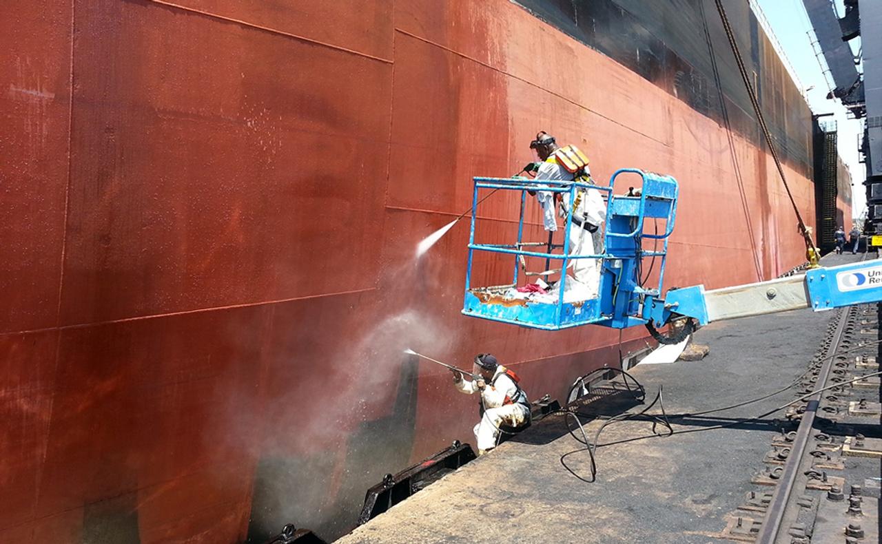 workers cleaning the side of a ship