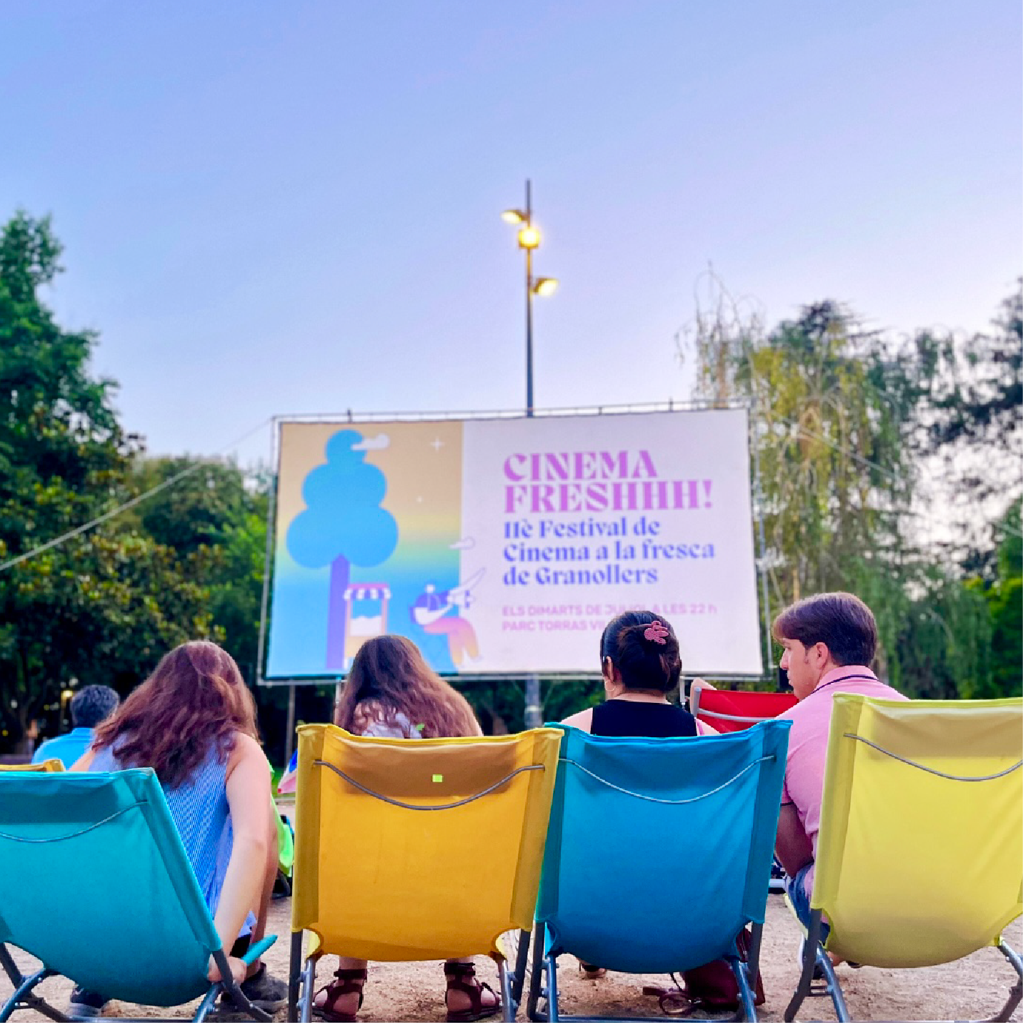 Grup de persones assegudes davant una pantalla de cinema on es projecta la imatge de la campanya "Granollers a la fresca" de Biombo Studio