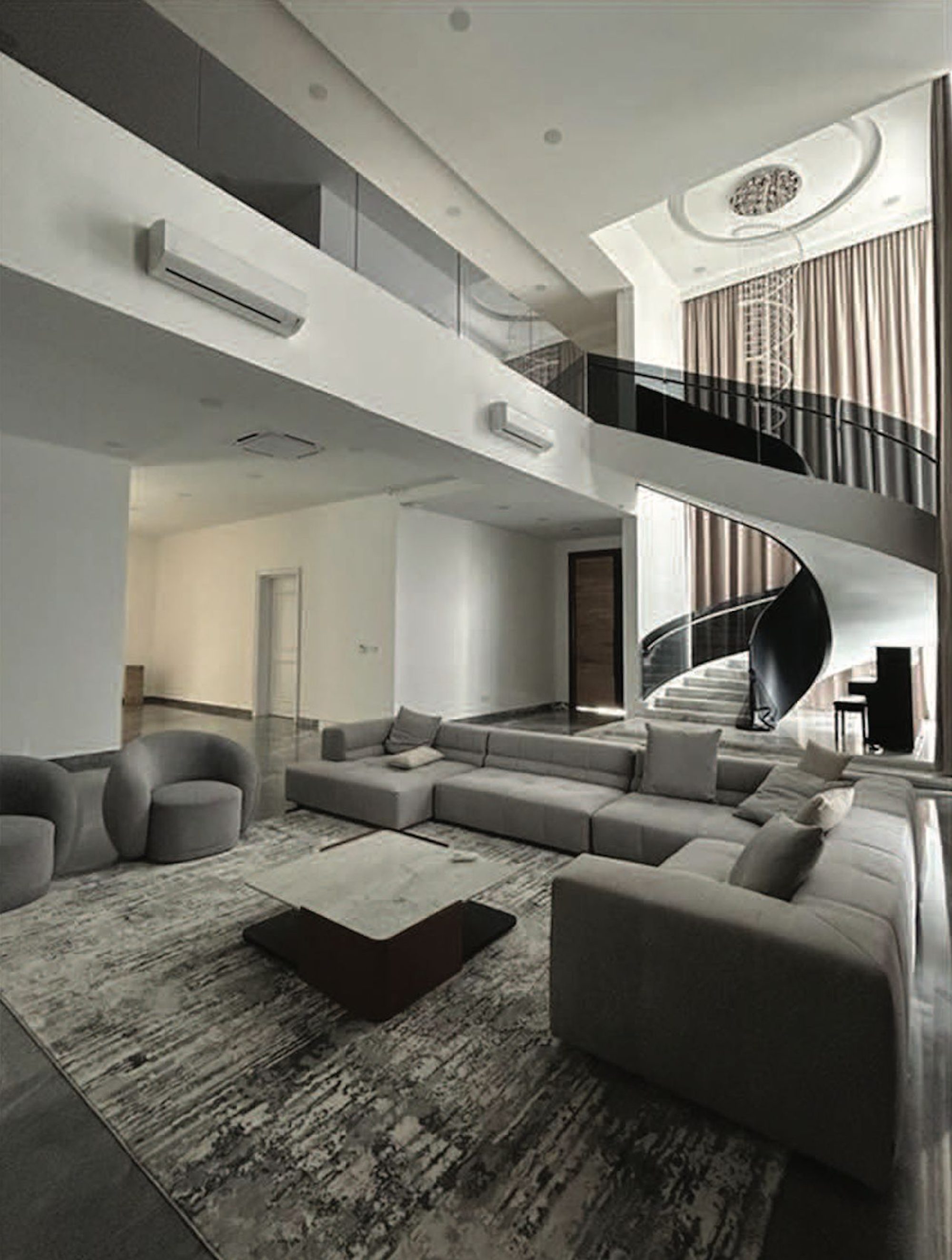 Double-height living hall with a sectional sofa and a spiral staircase with a black glass balustrade rising to a gallery