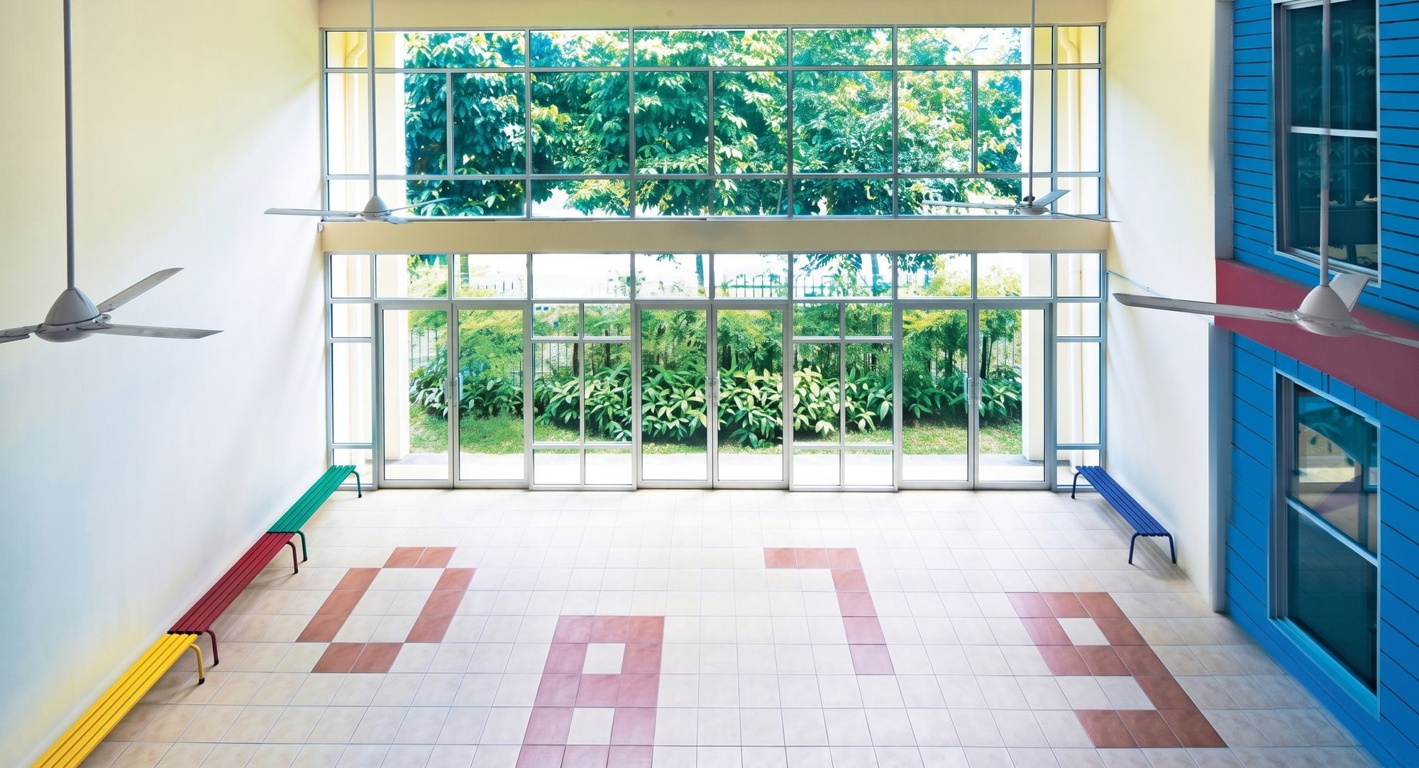 Assembly hall opening onto garden views through full-height glazing, with colourful benches