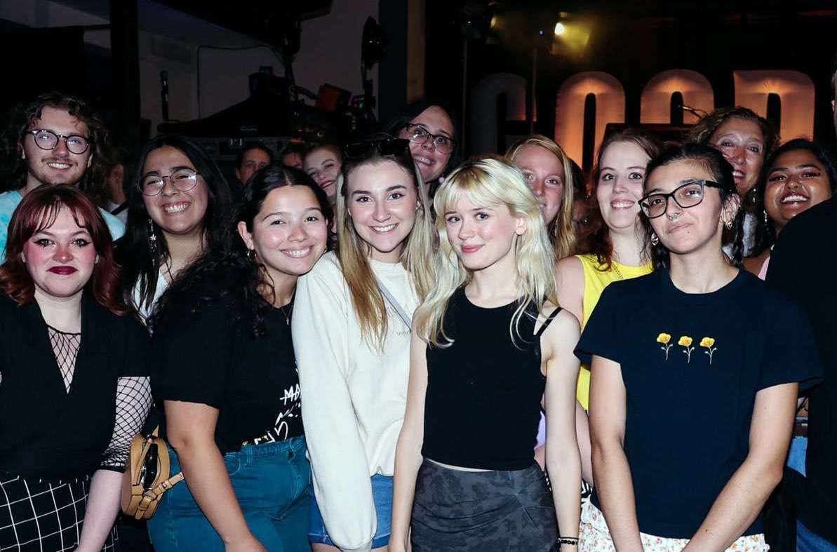 Blonde-haired singer Maisie Peters poses with smiling young fans.
