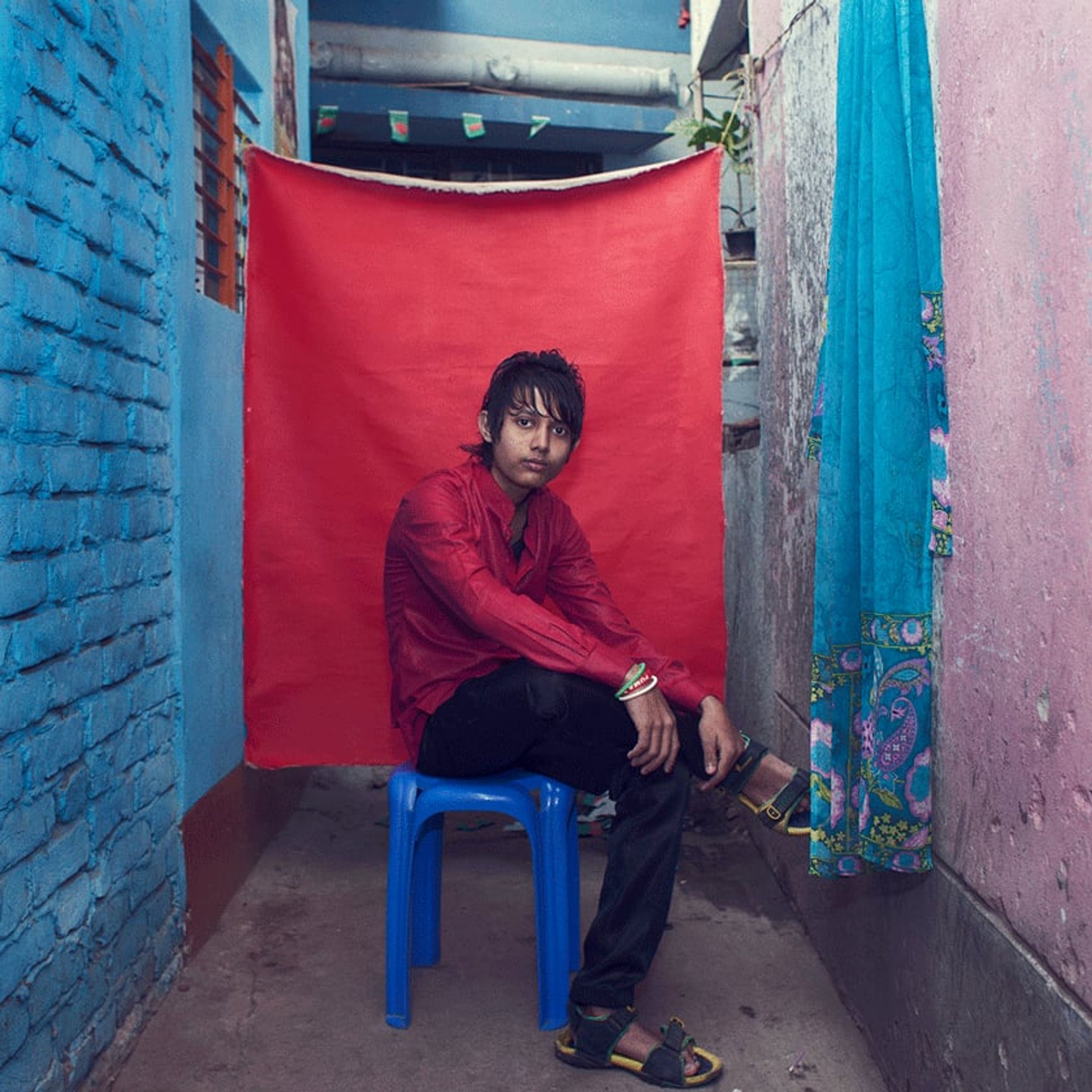 Young person in a red shirt sits on a blue stool before red fabric.