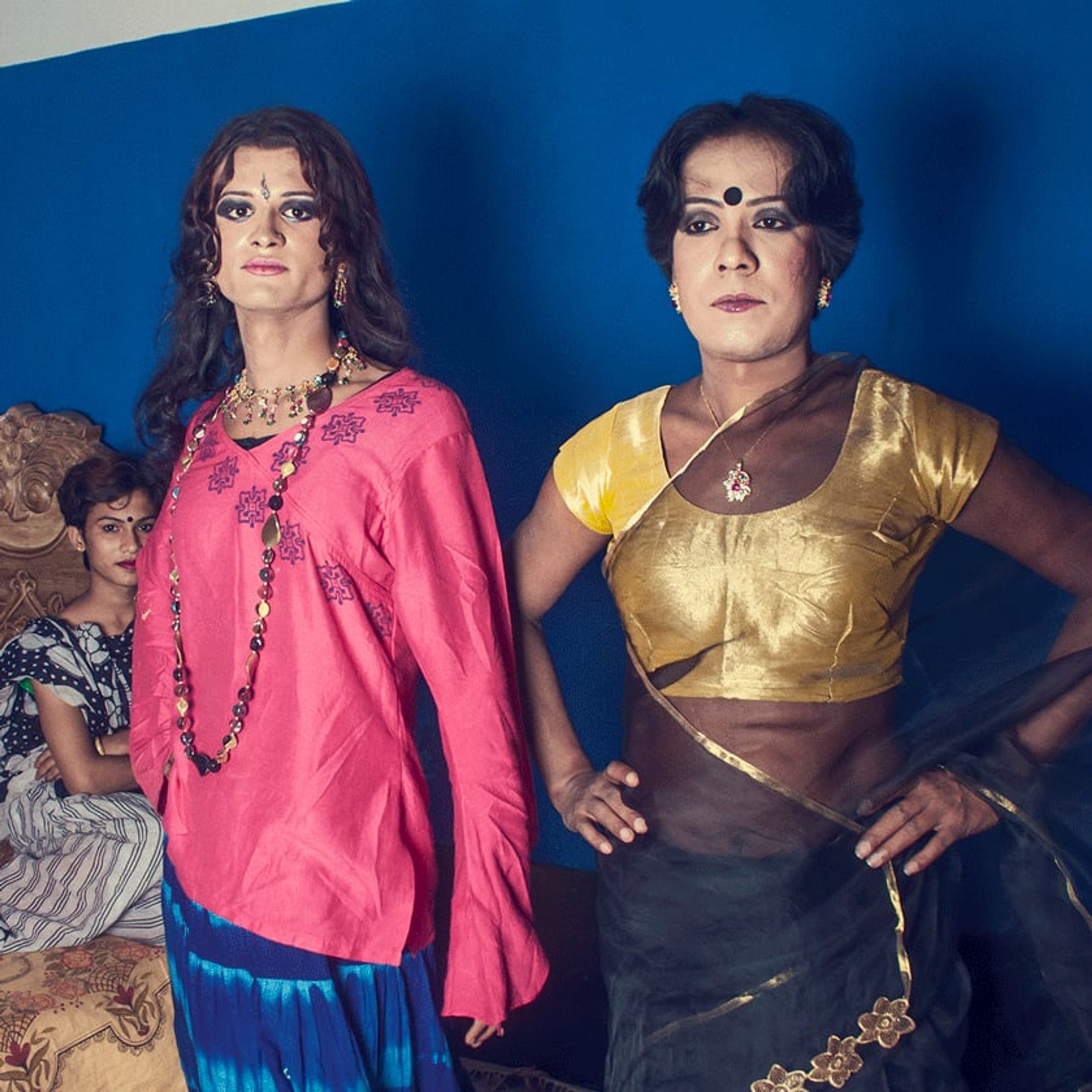 Two adults in bright pink and yellow clothing pose with hands on hips against a blue backdrop.