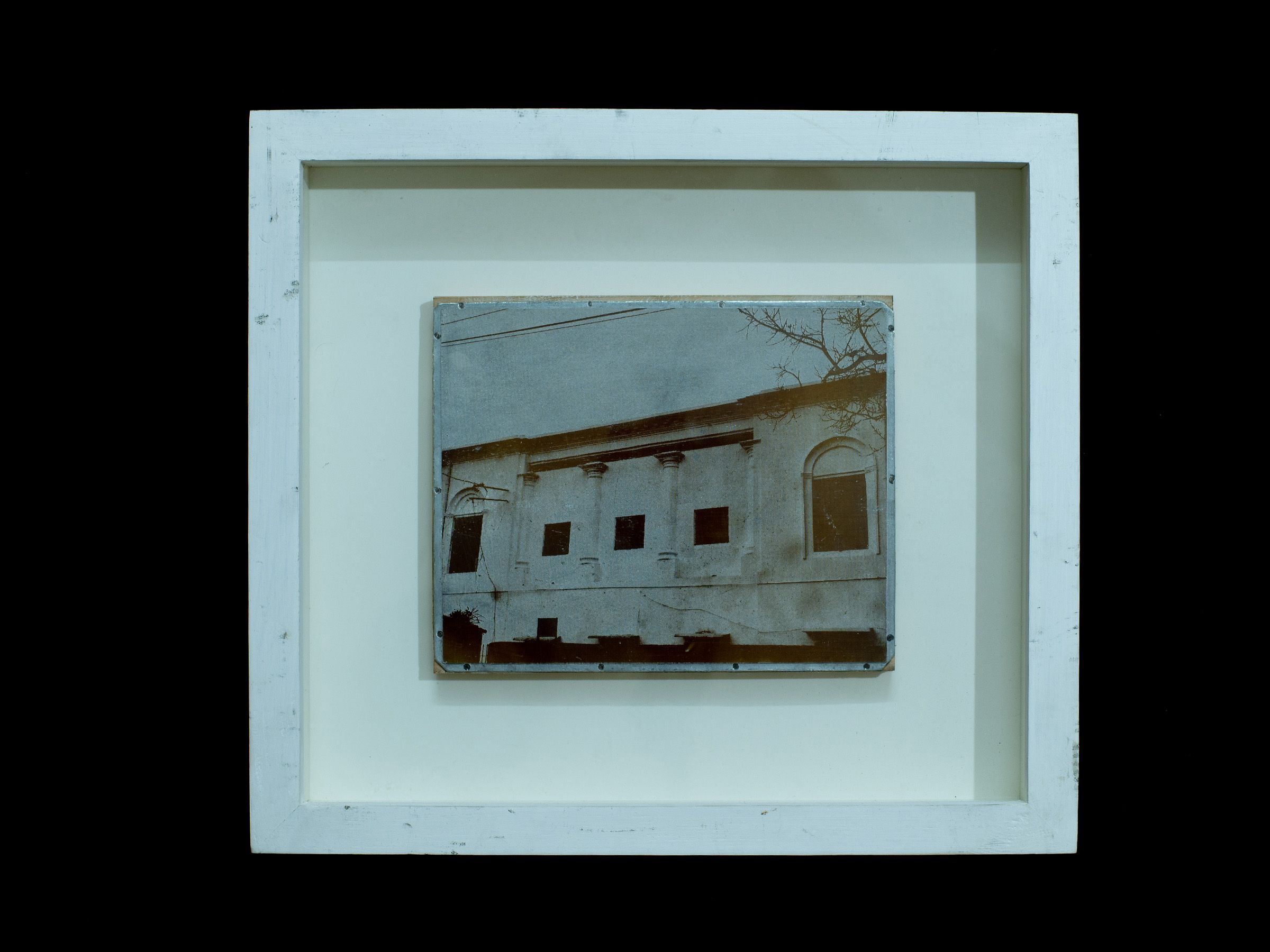 Small zinc plate depicting a long white masonry building displayed in a white frame.