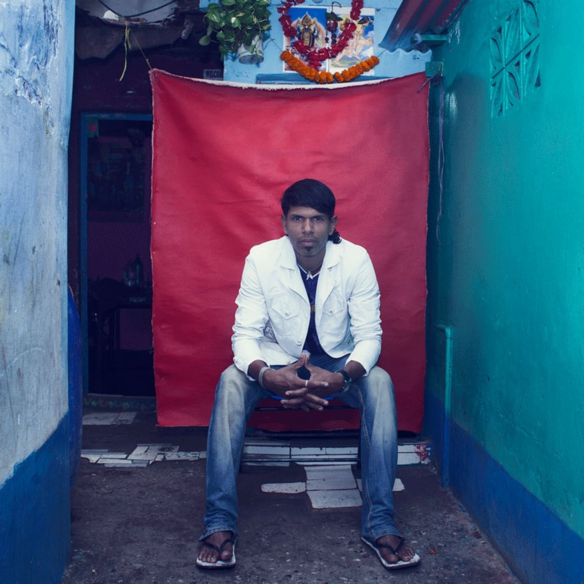 Young adult in a white jacket sits forward with hands clasped before red cloth.